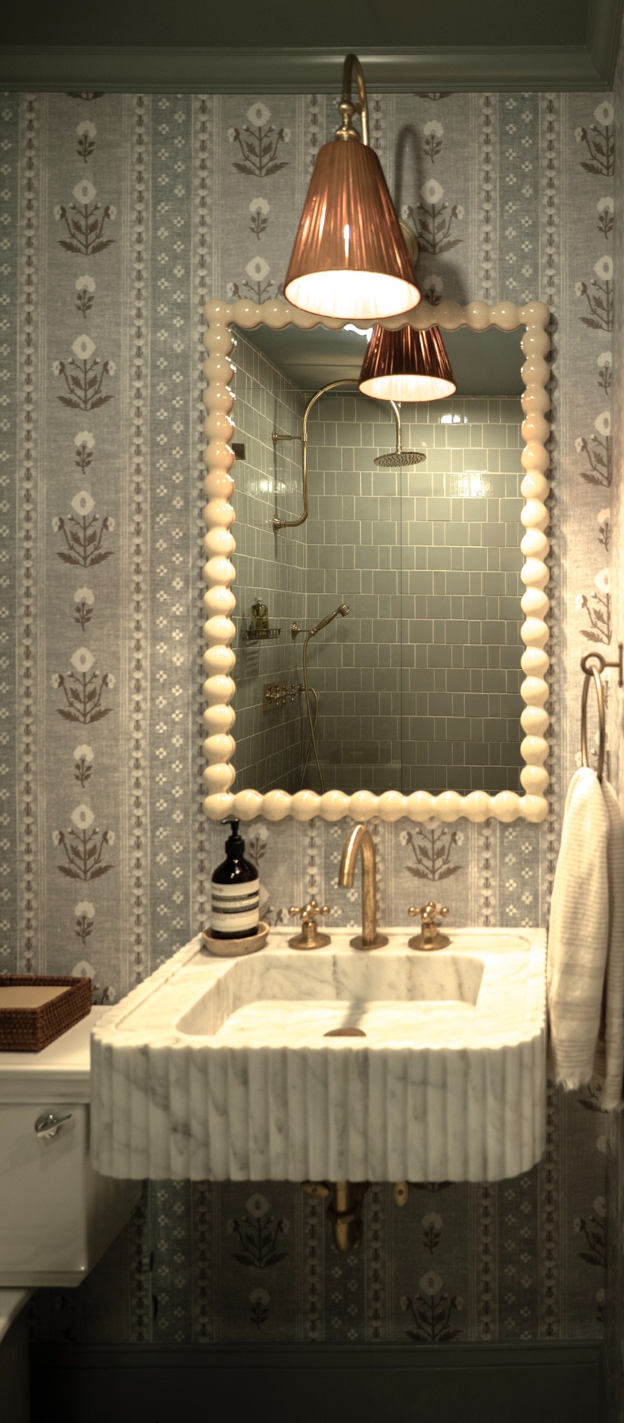 A scalloped mirror reflecting a tiled shower, framed in glossy cream