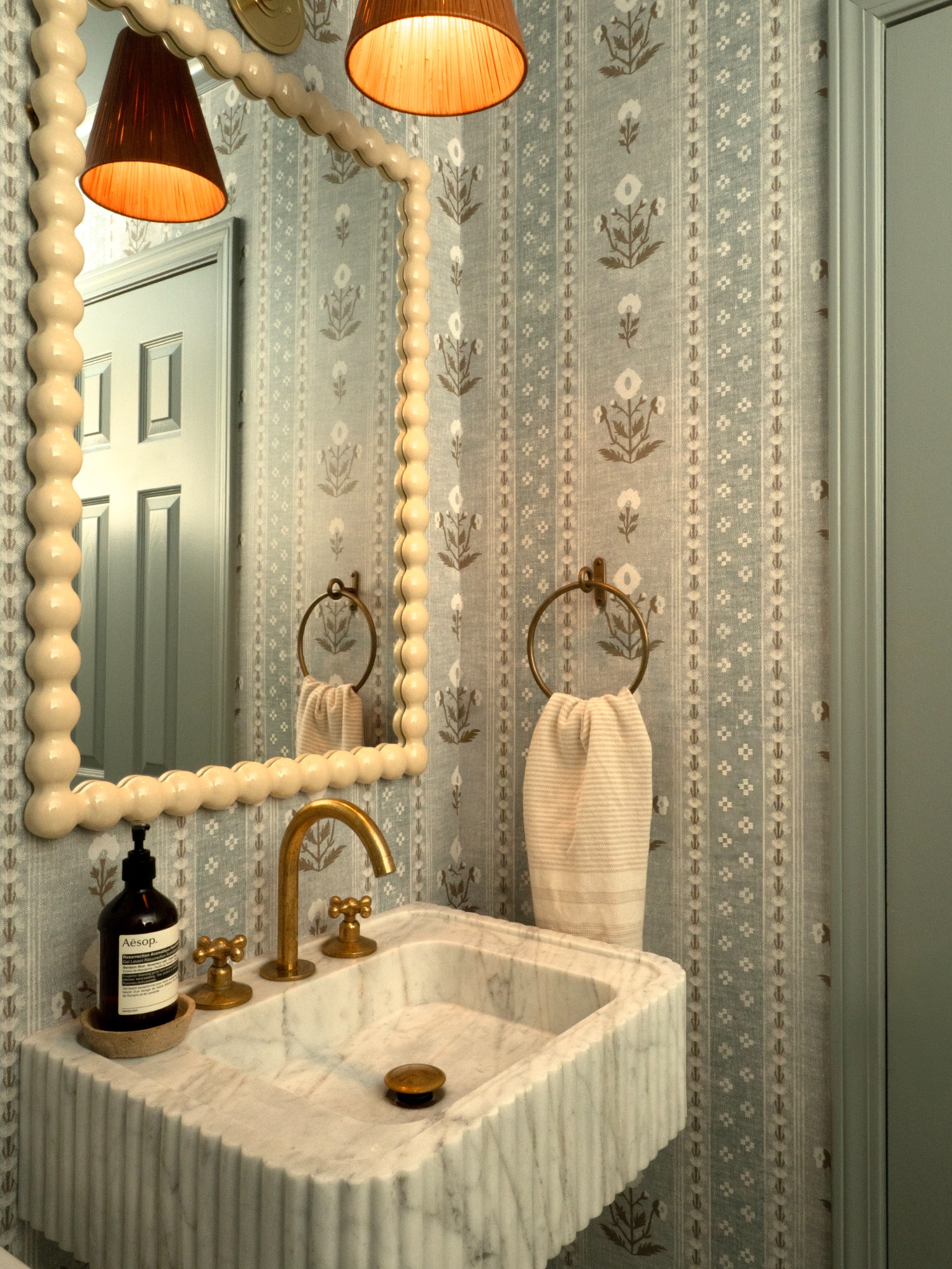 Blue floral powder room with scalloped mirror and marble sink in Harbor House, Westport, Connecticut