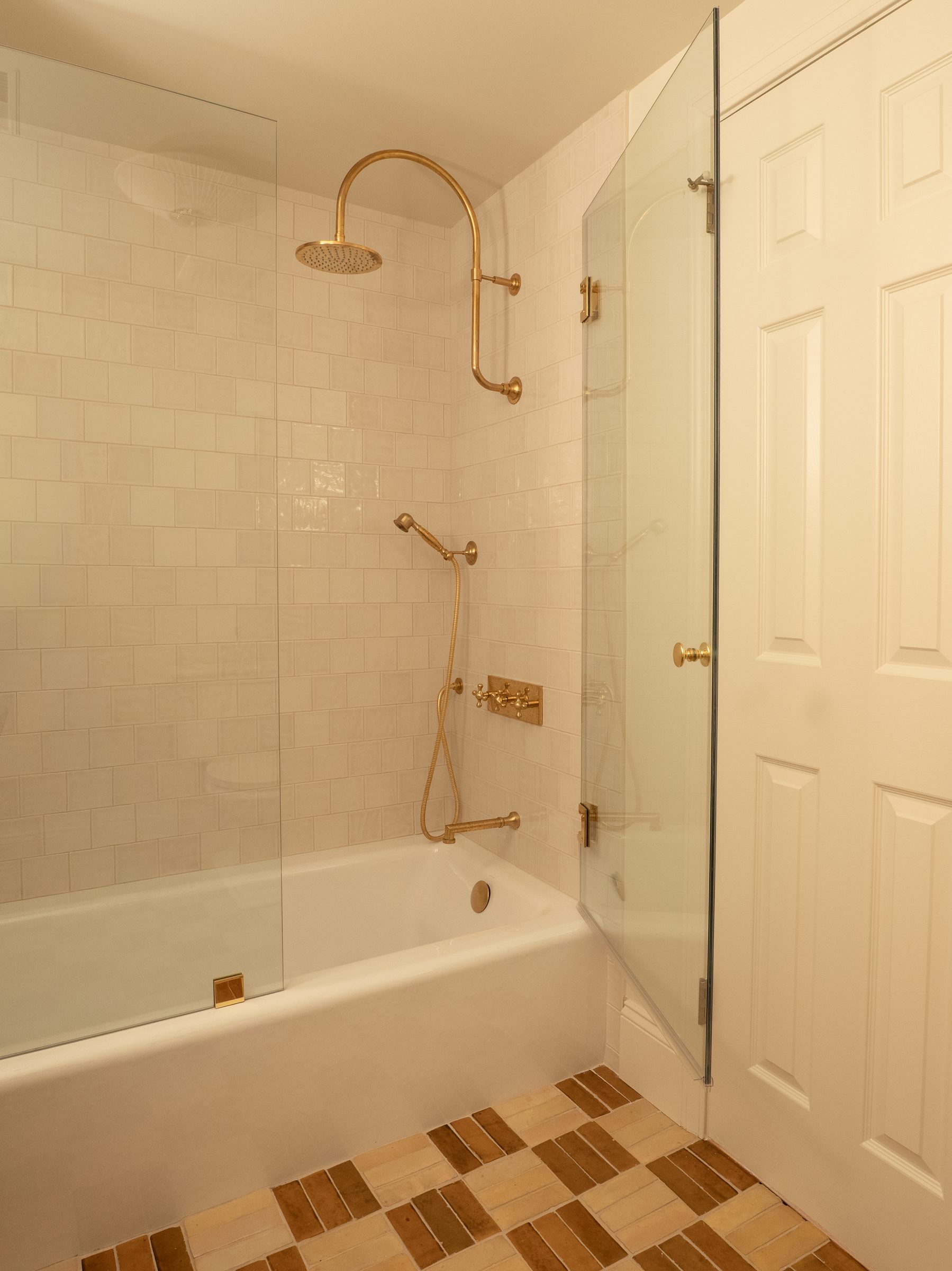 A tub and shower with brass fixtures and a terracotta tile floor