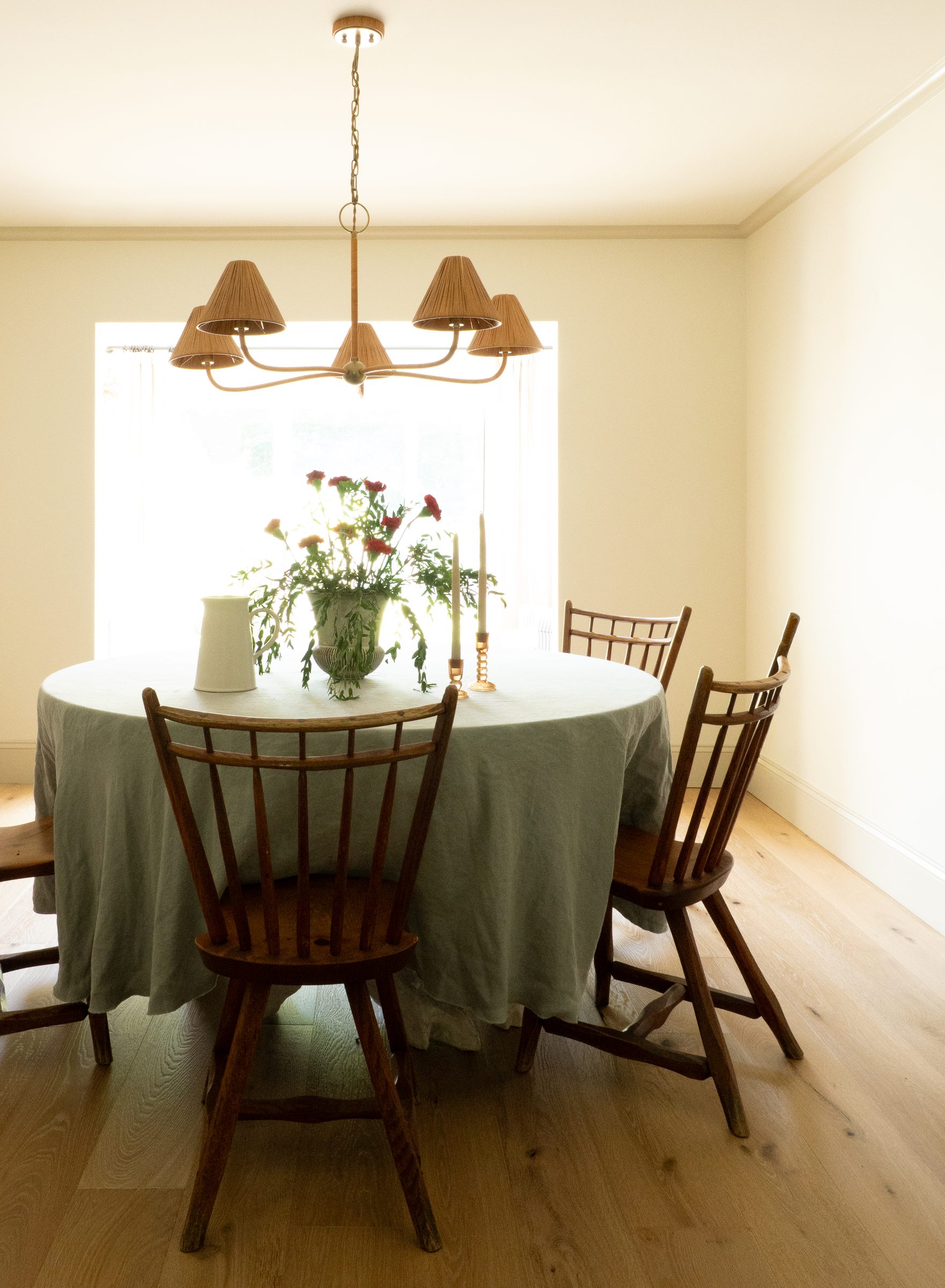 A round dining table set with linen and a brass chandelier overhead