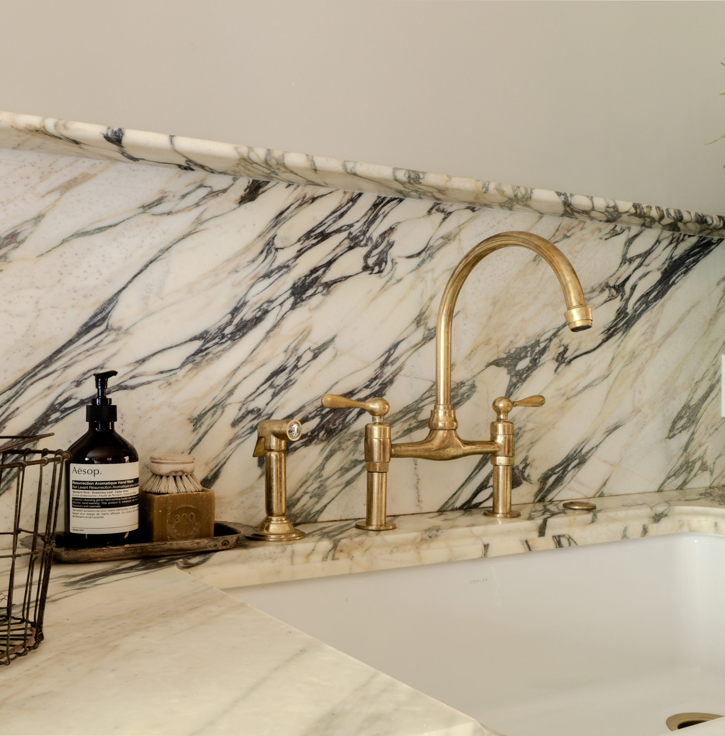 A brass bridge faucet against a veined marble backsplash