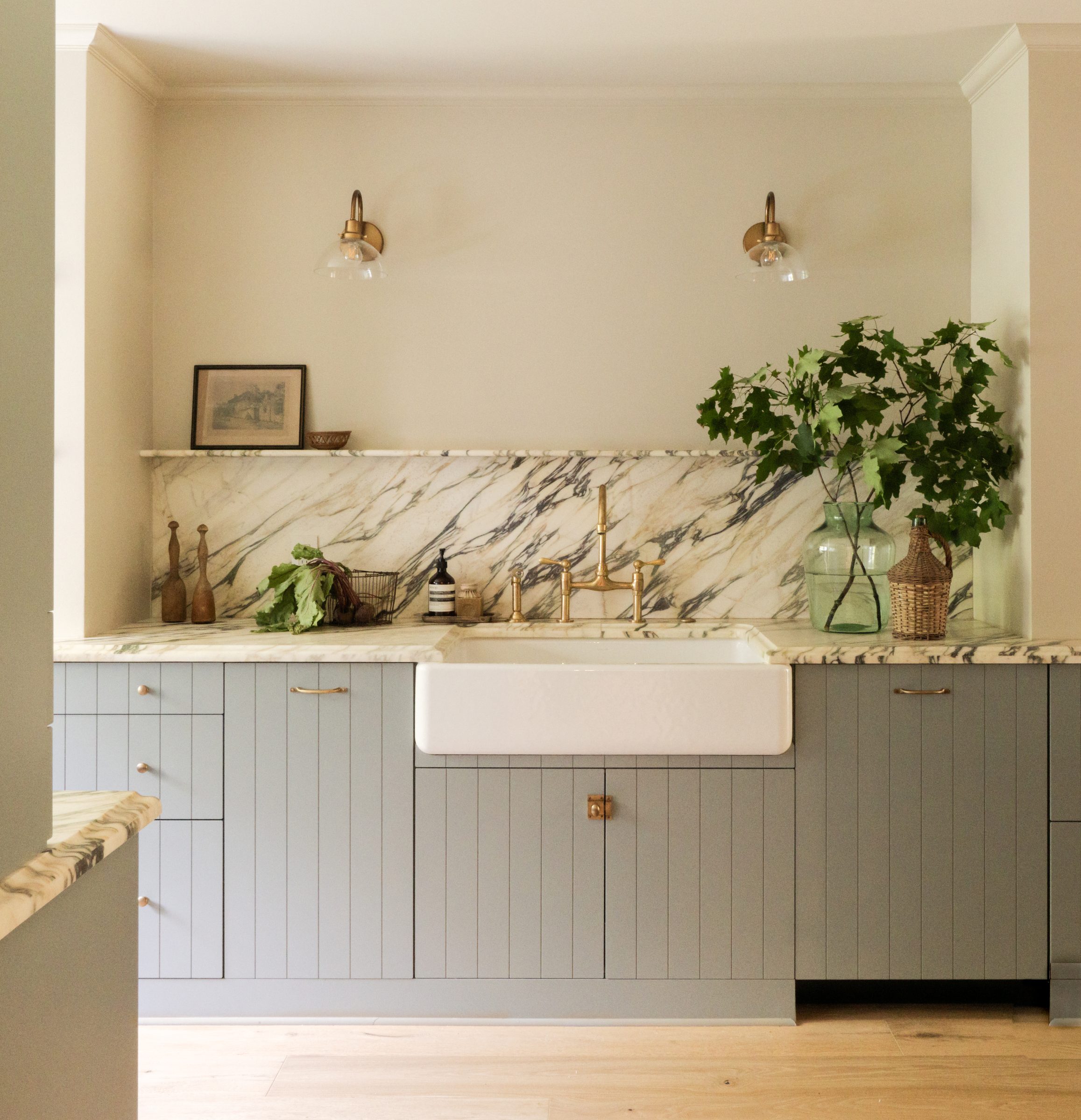 The sink wall with brass sconces, marble backsplash, and a potted plant