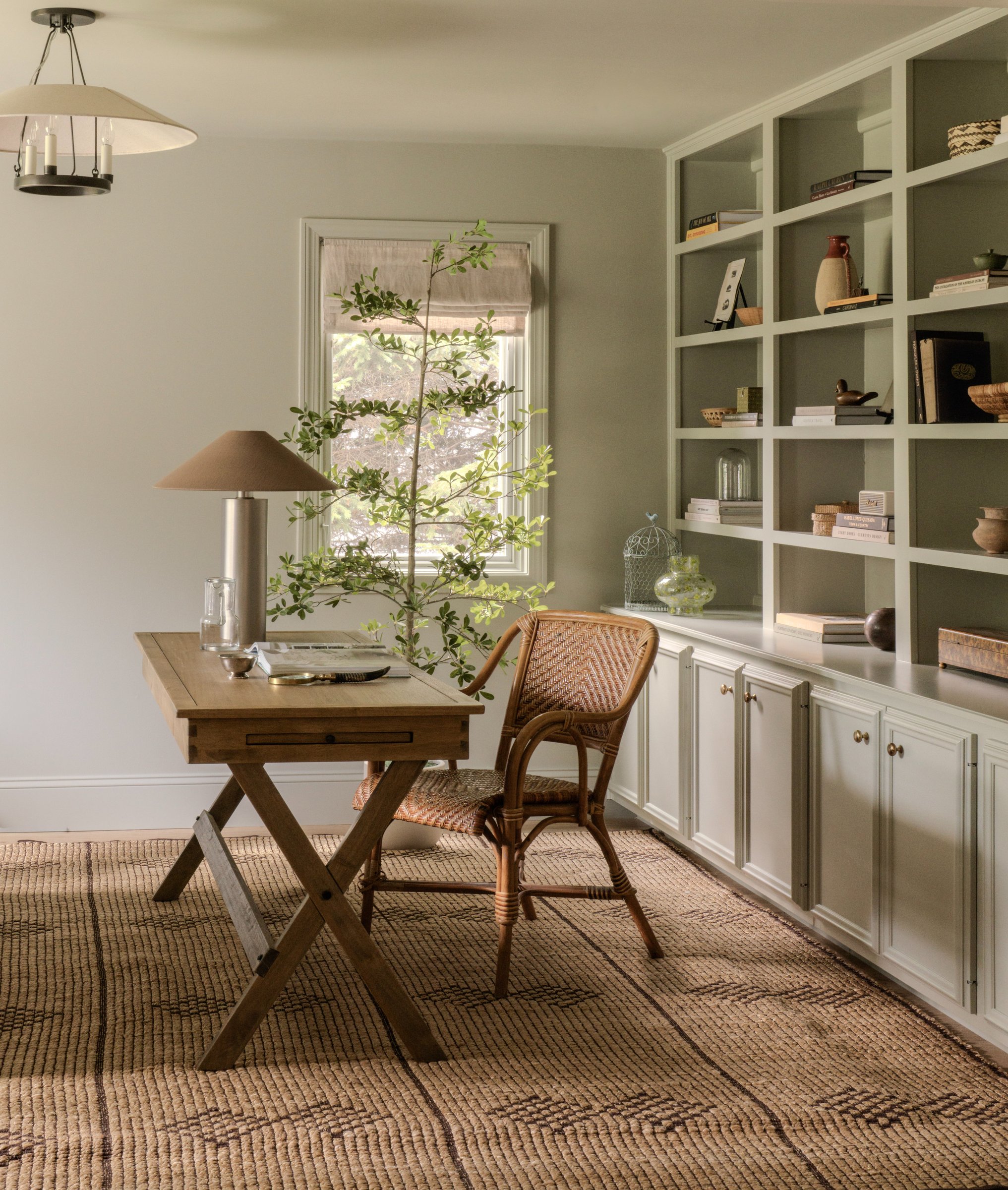A study with a drafting-style desk, a rattan chair, and built-in bookshelves